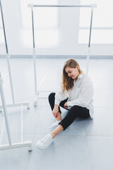 Fototapeta na wymiar Playful self-confident woman in a stylish cotton white shirt, black jeans, white leather sneakers, casual style.Blond-haired woman on a gray background in stylish clothes