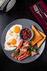 Full English Breakfast on dark table sausage eggs bean bacon tomatos mushroom