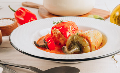 Pepper stuffed with minced chicken meat and rice in a white plate on a white wooden table.
