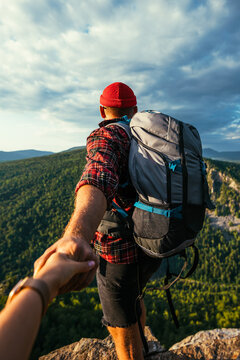 Portrait of a man holding his woman's hand while walking along a mountain range, vertical photo. The couple is enjoying a walk in nature. A girl holds her boyfriend's hand in the mountains. Follow me
