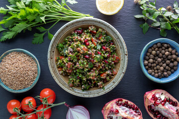 Tabbouleh salad with ingredients: bulgur, parsley, mint, pomegranate, lemon, tomato, onion, allspice. Top view.