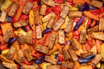 Baked tofu with vegetables background texture. Vegan dish top view.