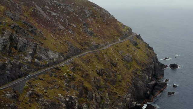 Breath taking shot of slowly moving car on narrow panoramic route in steep slope above sea coast. Dangerous road around Slea Head. Ireland