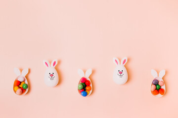 Top view festive Easter beige peach color background with funny bunny eggs containers filled with candy chocolate eggs. Bunny rabbit symbol. Easter egg hunt. Creative Easter. Color of the 2024 year.