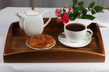 a cup of tea with a bun and a rose on a tray