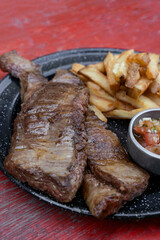 Grilled meat dish. Closeup view of skirt steaks with french fries and criolla sauce, in a black dish.