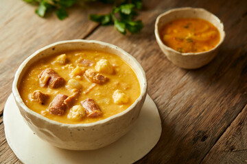 Mote pata is a traditional ecuadorian soup made from mote, pork, sausage and sambo seeds. It’s served on a white plate with a rustic, wooden and homey background. 