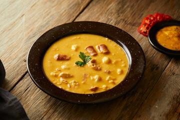Mote pata is a traditional ecuadorian soup made from mote, pork, sausage and sambo seeds. It’s served on a white plate with a rustic, wooden and homey background. 