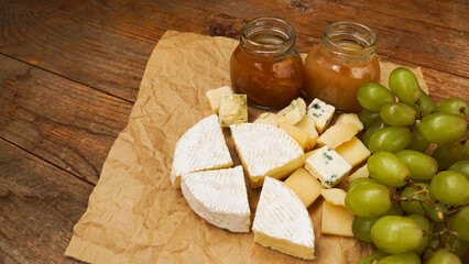 Camembert and other types of cheese and green grapes on craft paper with home made jam and honey in glass jar, food concept