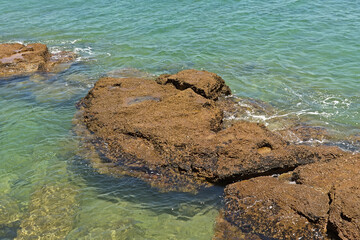 brown rock in blue reppling water of the sea
