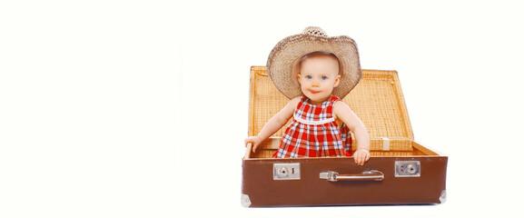 Portrait of cute smiling baby in straw summer hat sitting in suitcase on white background