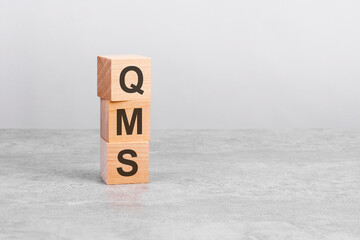 wooden cube on a table with text QMS. copy space on right for design, gray background
