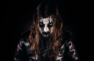 Portrait photo of black metal metalhead man with long brown hair and painted face standing in...