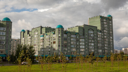 Ein riesiges grünes Wohnhaus im russischen, stalinistischen Baustil mit türkisen Kuppelnn auf...