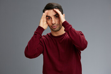 successful man covers face with hands in a red sweater gesturing with hands posing Gray background