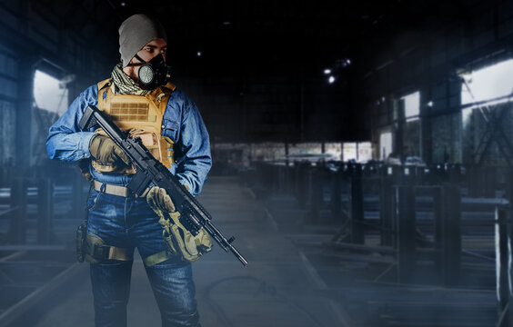 Photo of urban soldier in tactical military outfit and gas mask standing with rifle and gas mask on dark factory background.