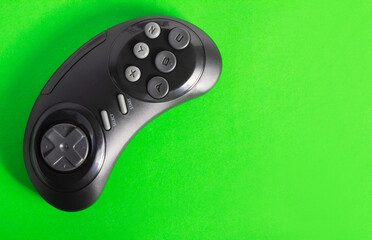 Close up photo of classic wireless black colored 16 bit game pad controller laying on green...