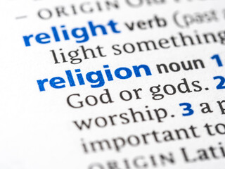 Religion - English dictionary definition of the word - photo of a dictionary page with paper grain texture - selective focus on the word