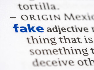 Fototapeta premium Fake - English dictionary definition of the word - photo of a dictionary page with paper grain texture - selective focus on the word