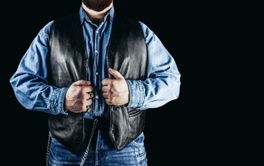 Front view photo of man in jeans shirt, denim pants and leather biker vest standing on black...