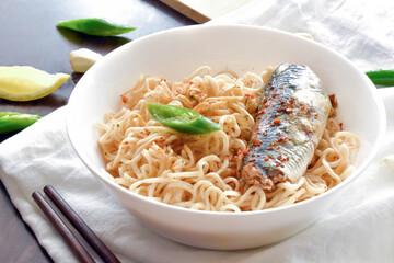 Instant noodles with sardine, red chilli flakes and seasonings in a white bowl.
