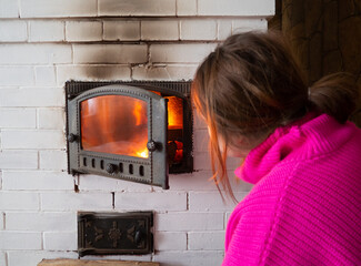 girl throws firewood into the fire in the stove. Furnace firebox in the house. Lighting a fire in...