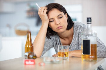 depressed young woman drinking alcohol and smoking cigarette at home