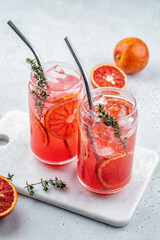 Blood Orange lemonade cocktail with ice and thyme on light gray concrete background