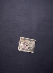 Metal banknote clip with US ten-dollar paper currency on black leather background with a lot of copy space for design	