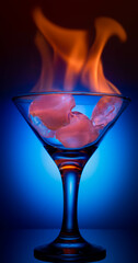 Fire on the wine glass, glass of martini with ice on a dark navy blue background and fire, ice cubes on fire