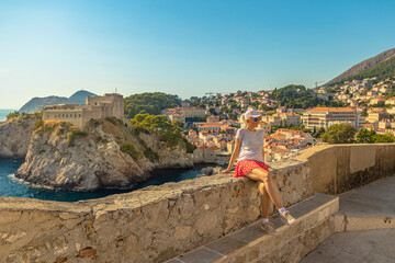 Woman sitting on top walls of Dubrovnik city of Croatia. Looking Fort Lovrijenac fortress, over the...