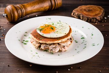 A stack of buckwheat pancakes with mushroom sauce and fried eggs on a wooden background. Tasty and healthy breakfast
