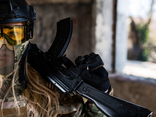 Portrait of a woman in a helmet and goggles with a machine gun in her hands. A female soldier in a camouflage uniform holds a weapon.