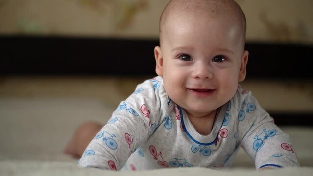 Newborn Active Baby Cute Smiling Teethless Face Portrait Early Days On Stomach Developing Neck Control. 5 Months Child On White Bed Looking on Camera. Infant, Childbirth, Parenthood, Beginning Concept