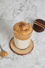 Frappé, cold coffee with milk in a glass on a wood and marble table. Spoon with dulce de leche, salted caramel and alfajores behind. View from above.
