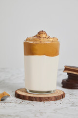 Frappé, cold coffee with milk in a glass on a wood and marble table. Spoon with dulce de leche, salted caramel and alfajores behind