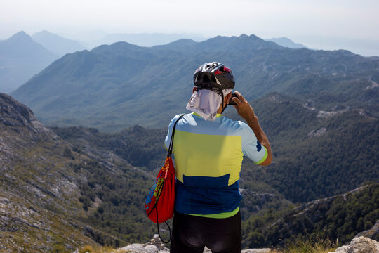 Man in cycling clothes and helmet takes photo of mountain landscape on his phone