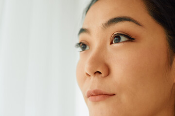 Close-up of young Asian woman by the window looking away.