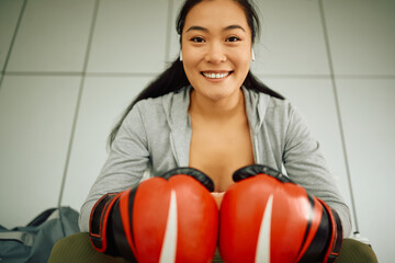 Young happy Asian female boxer in locker rom looking at camera.