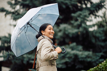 Young happy Asian businesswoman with an umbrella walking in the city. © Drazen
