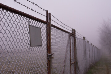 Barbed wire fence and locked gate on a misty winter day.