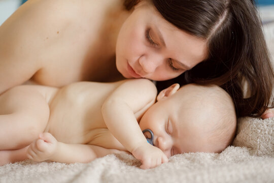 a beautiful naked baby sleeps near his mother on bed. happiness of motherhood.