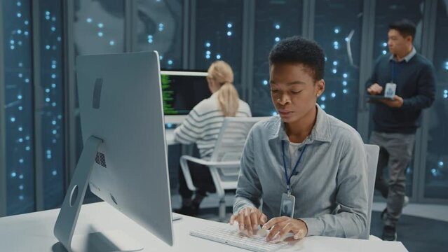 Data center. Afro-american young woman using computer desktop and cooperating with IT administrator. Futuristic server room. Management. Staff.