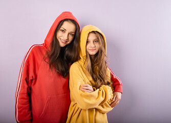 Happy smiling beautiful young mother and cute daughter posing in fashion trendy yellow and red hoodie together on purple studio background with empty copy space. Happy loving