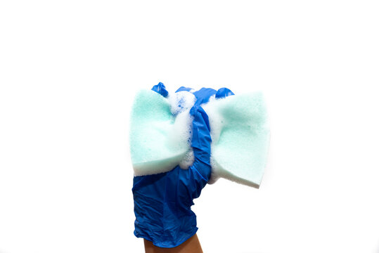 Mano con guantes Vinilo azules exprimiendo una esponja azul con mucha espuma blanca sobre un fondo blanco