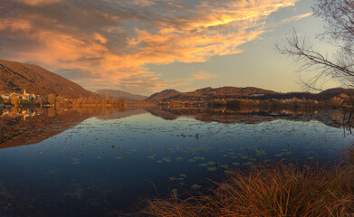 Vllage of Santa Maria overlooking the lake in the middle of hills during an autumn sunset. Revine Lakes, Veneto, Italy. Concept about reflection and relaxation