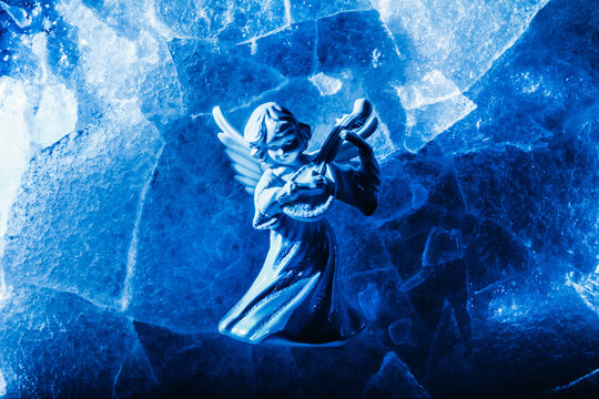 Photo of blue toned ice angel miniature playing the lute and laying on cracked ice surface backdrop.
