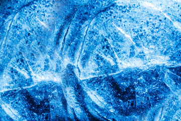 Close up photo of blue toned frozen circle cracked ice surface texture.