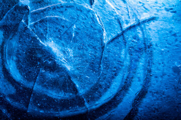 Close up photo of blue toned frozen circle cracked and damaged ice surface texture.