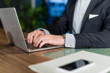 partial view of man in suit typing on laptop keyboard in hotel lobby, banner